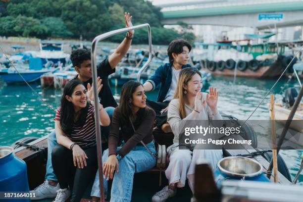 young tourists of mixed nationalities waving goodbye to the fishermen passing by - waving stock pictures, royalty-free photos & images