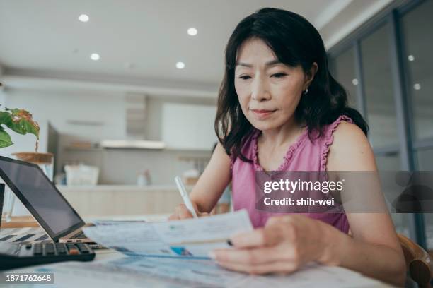 eine frau ist zu hause und hält eine sammlung von papierrechnungen und finanzplänen in der hand. sie scheint sich darauf zu konzentrieren, ihre persönlichen finanzen zu verwalten, möglicherweise rechnungen zu sortieren, budgets zu erstellen oder ihre f - sparpaket stock-fotos und bilder