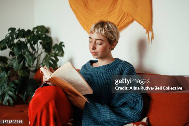 young woman reading a book on a couch - lit photos et images de collection