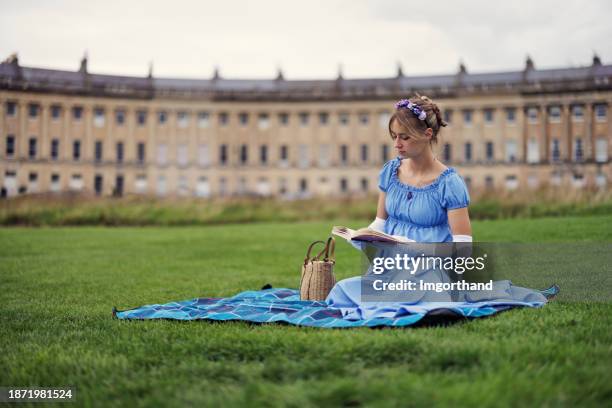 junge frau in einem kleid aus der regency-ära liest ein buch in einem öffentlichen park vor dem royal crescent - regency stil stock-fotos und bilder