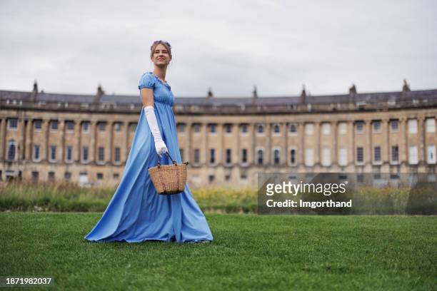 young woman wearing a regency era dress is walking in a public park in front of royal crescent - girl in blue dress stock pictures, royalty-free photos & images