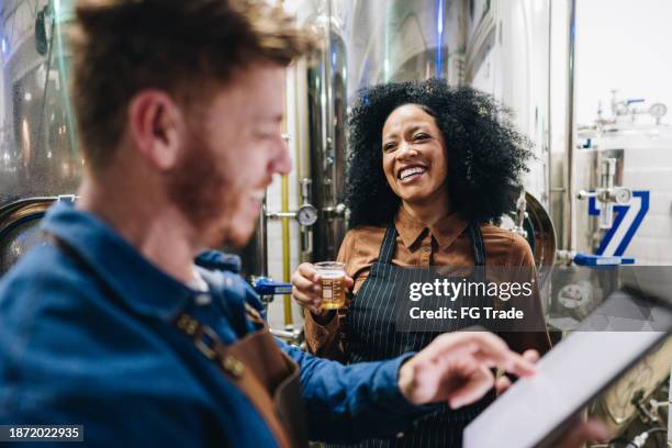 coworkers talking and analyzing a glass of beer at brewery - distillery stock pictures, royalty-free photos & images