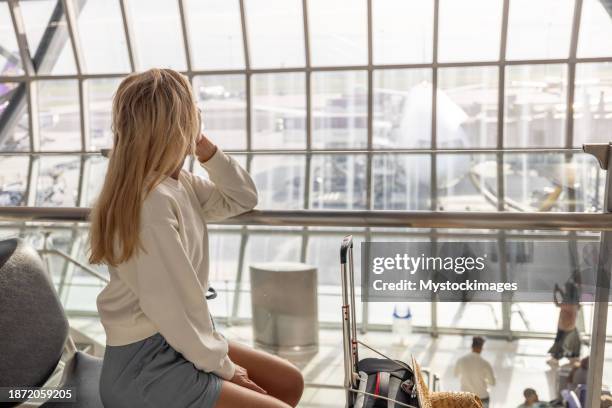 woman at the waiting area in the airport, she looks through window - woman blond looking left window stockfoto's en -beelden