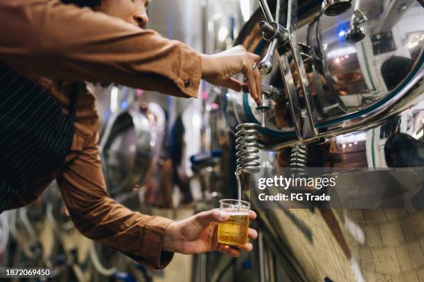mujer que vierte cerveza en vaso para examinar en cervecería - destilación fotografías e imágenes de stock