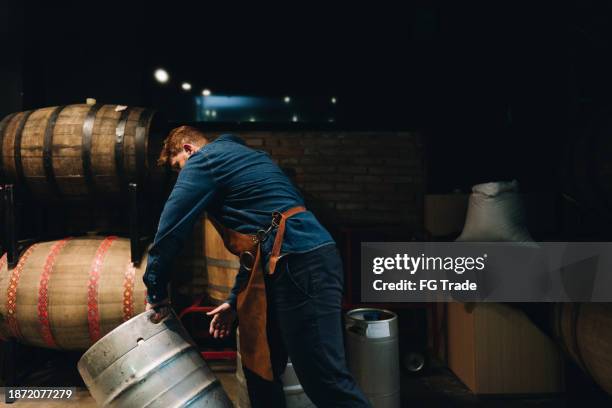 man picking up a barrel of beer at microbrewery - distillery stock pictures, royalty-free photos & images