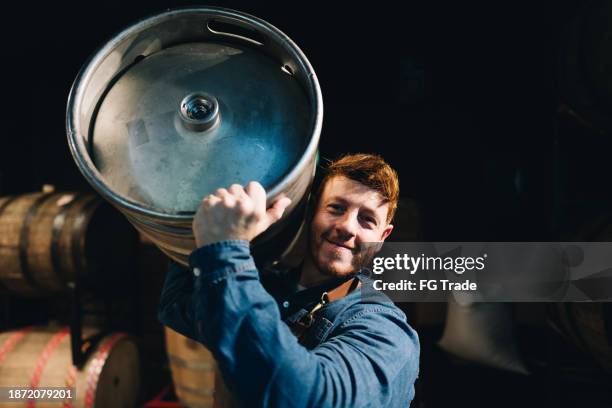 porträt eines reifen mannes, der in einer mikrobrauerei ein bierfass auf den schultern trägt - bierfass stock-fotos und bilder