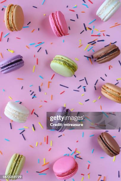 full frame image of group of multi coloured macarons filled with flavoured butter cream standing on edge, strawberry, vanilla, blueberry, orange, pistachio, chocolate flavoured meringues, spilled sugar sprinkles, purple background, elevated view - fondant stock pictures, royalty-free photos & images