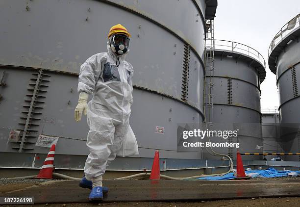 Tokyo Electric Power Co. Employee wearing a protective suit and a mask walks past storage tanks for radioactive water in the H4 area at the Fukushima...