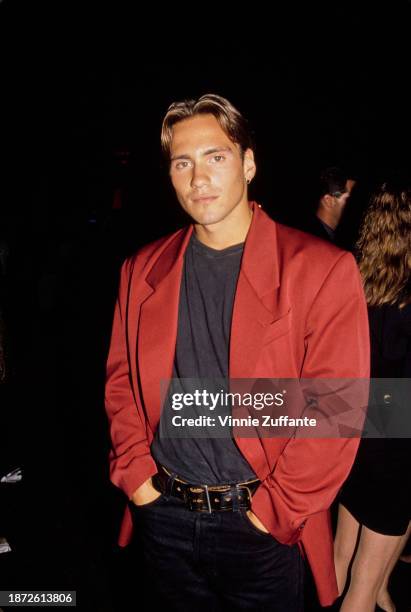 American fashion model and television personality Eric Nies, wearing a red jacket over a black crew neck top and black trousers, attends the 1992 MTV...