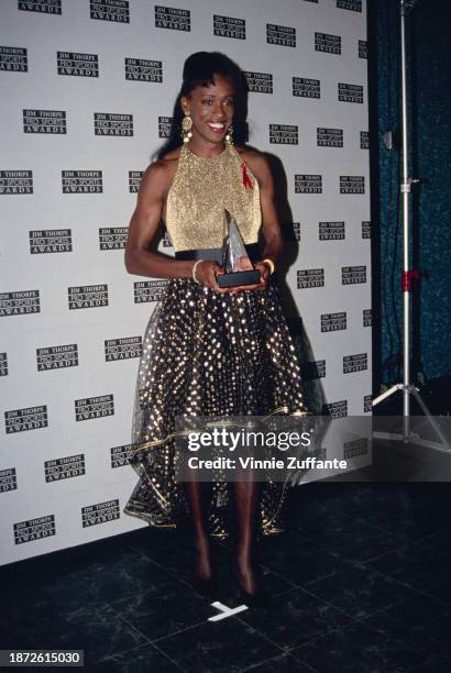 American heptathlete Jackie Joyner-Kersee, wearing a sleeveless gold top with a black-and-gold skirt, in the press room of the 2nd Annual Jim Thorpe...