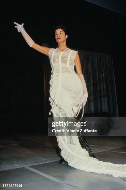 Fashion model walks the runway, wearing a white dress with a long white train and white evening gloves, an outfit designed by French fashion designer...