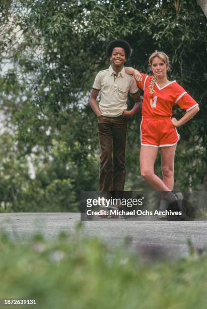 American actor Todd Bridges, wearing a beige short-sleeve polo shirt and brown trousers, standing on a skateboard, beside American actress Dana...