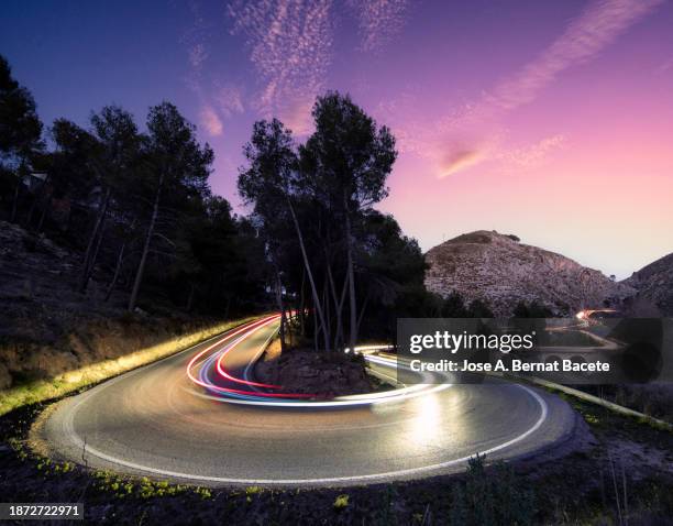 road with an elliptical curve and light trails of moving cars at sunset. - hairpin curve stock-fotos und bilder