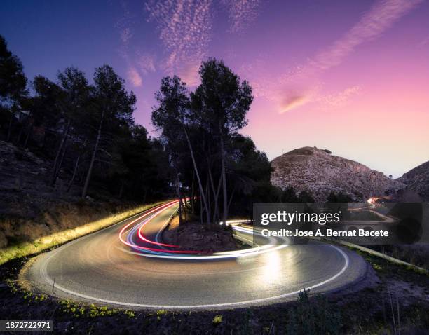 road with an elliptical curve and light trails of moving cars at sunset. - hairpin curve stock pictures, royalty-free photos & images