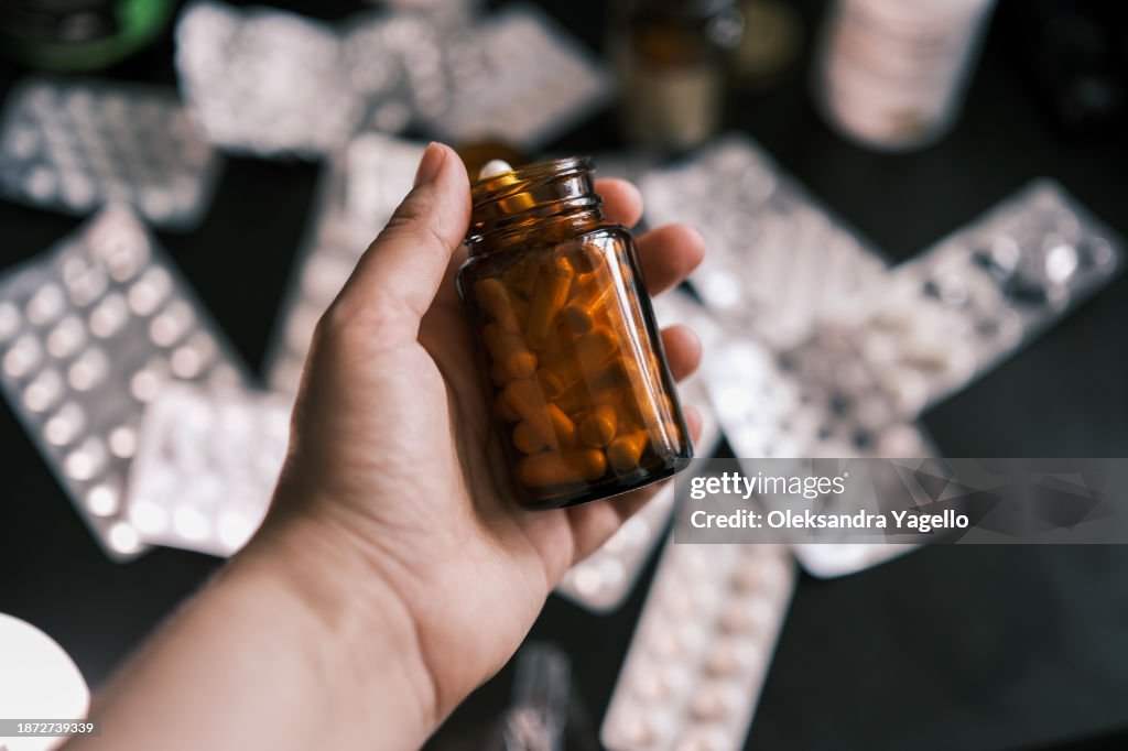 Jar with pills in hand. Different types of tablets in packages and jars on the table.