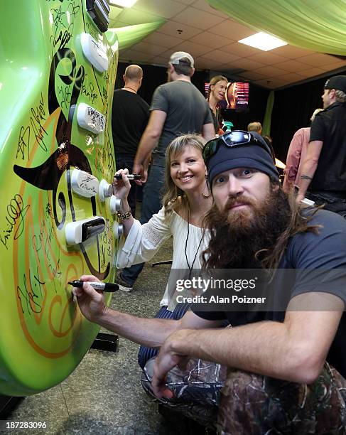 Missy Robertson and Jase Robertson of Duck Dynasty sign a giant Patron tequila guitar backstage at the CMA Awards to benefit the "Keep the Music...