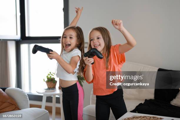 deux sœurs enfants de jouer aux jeux vidéos à la maison ensemble. childeren heureux, notion d’insouciance de l’enfance - command sisters photos et images de collection