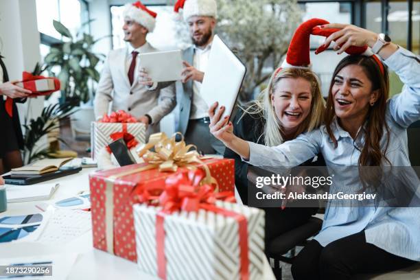 smiling females in office joining santa hats for a funny christmas selfie - father christmas stock pictures, royalty-free photos & images