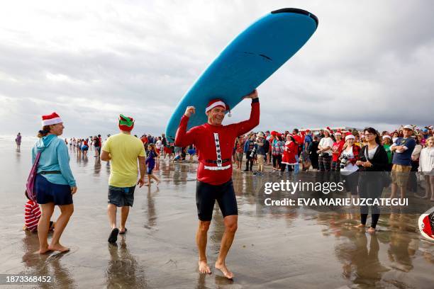 Surfer dressed as Santa carries his board during the 15th annual "Surfing Santas" event in Cocoa Beach, Florida, on December 24, 2023.