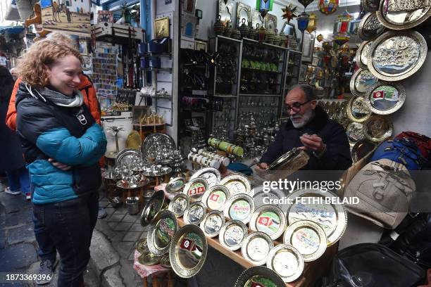 Tunisian artisan displays a copper plate he is engraving to a tourist at his shop in the souks of the medina of Tunis on December 7, 2023. The...