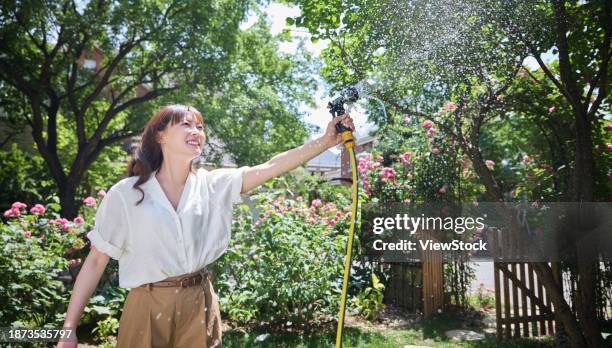 young beauty watering flowers in the courtyard - rosa hose photos et images de collection