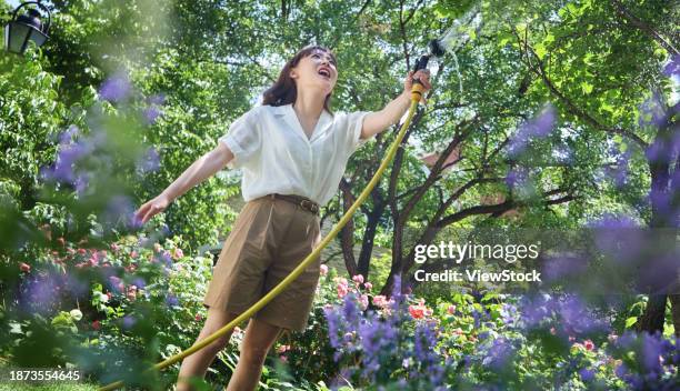 young beauty watering flowers in the courtyard - rosa hose photos et images de collection