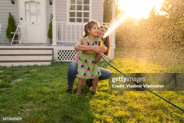 a mother and daughter watering the grass with hosepipe - hose stock pictures, royalty-free photos & images