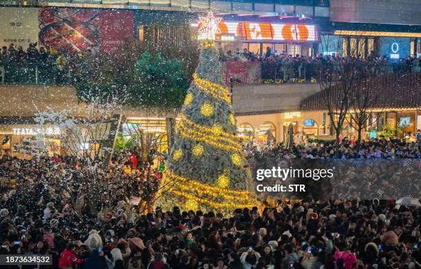 This photo taken on December 24, 2023 shows people gathering around a Christmas tree at a business area with artificial snow in China's southwestern...