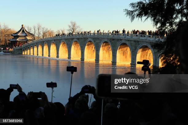 Tourists take photos as the sunset illuminating the arches of the 17-Arch Bridge at the Summer Palace on December 21, 2023 in Beijing, China.