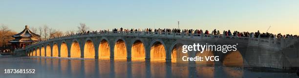 Tourists take photos as the sunset illuminating the arches of the 17-Arch Bridge at the Summer Palace on December 21, 2023 in Beijing, China.