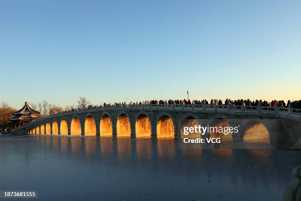 Tourists take photos as the sunset illuminating the arches of the 17-Arch Bridge at the Summer Palace on December 21, 2023 in Beijing, China.