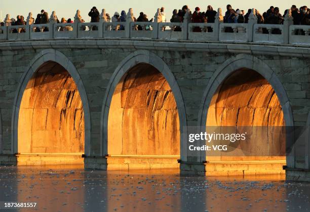 Tourists take photos as the sunset illuminating the arches of the 17-Arch Bridge at the Summer Palace on December 21, 2023 in Beijing, China.