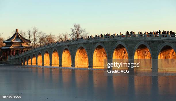 Tourists take photos as the sunset illuminating the arches of the 17-Arch Bridge at the Summer Palace on December 21, 2023 in Beijing, China.