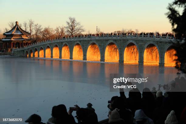 Tourists take photos as the sunset illuminating the arches of the 17-Arch Bridge at the Summer Palace on December 21, 2023 in Beijing, China.