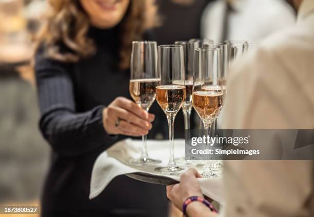 a bartender holds a plate with pink champagne and a woman in a cocktail dress takes one of the glasses at an event, party or wedding. - business introduction stock pictures, royalty-free photos & images