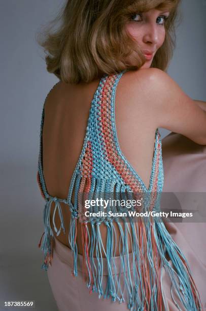 An unidentified model in a backless, crocheted top and pink skirt, glances over her shoulder, February 1975. The photo was taken as part of a fashion...