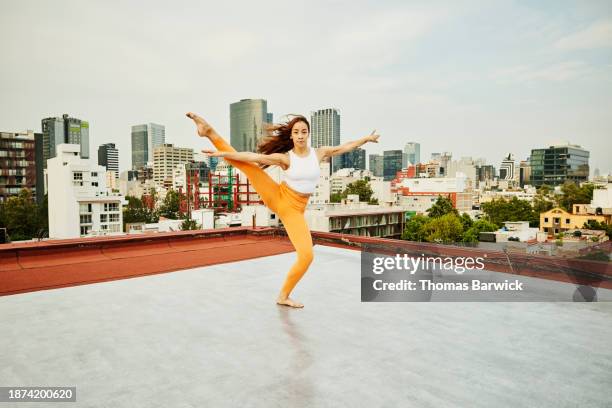 wide shot dancer balanced on one foot while performing on city rooftop - レギンス　 ストックフォトと画像