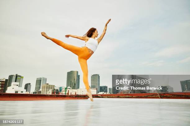 wide shot dancer jumping in mid-air while performing on city rooftop - レギンス　 ストックフォトと画像