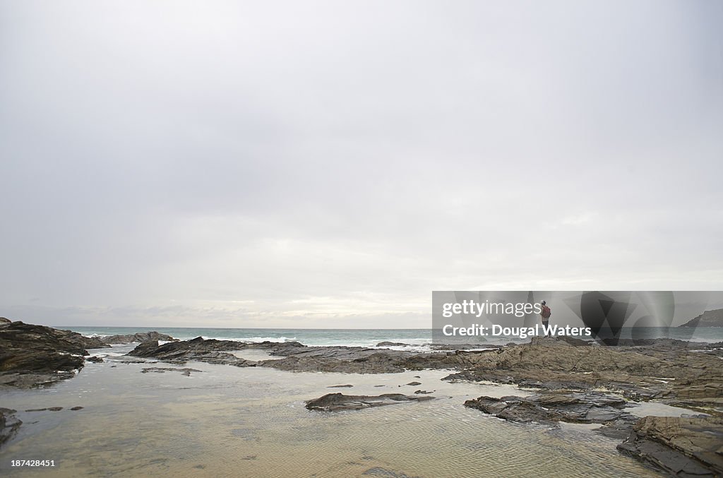 Hiker standing on coastal rocks in seascape.