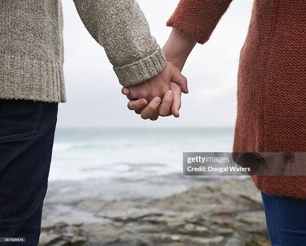 Close up of couple holding hands on coastline.