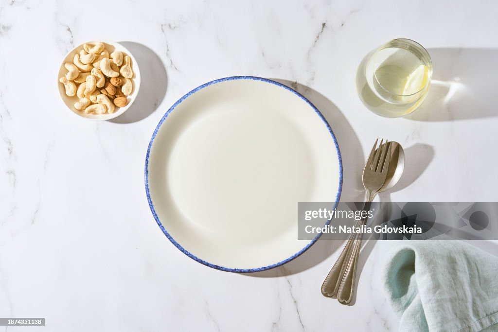 Clean empty white plate, glass of water, fork and spoon on white stone table, copy space