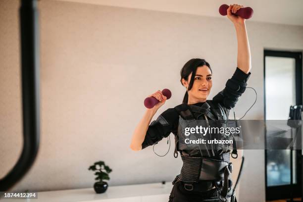 young woman training with dumbbells while wearing an ems suit - ems stockfoto's en -beelden