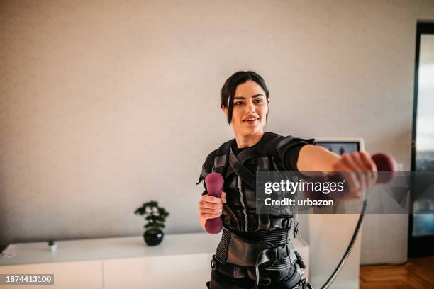 young woman training with dumbbells while wearing an ems suit - ems stockfoto's en -beelden