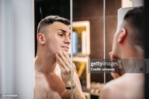 junger mann, der sich im badezimmerspiegel ansieht - eitelkeit stock-fotos und bilder