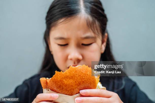 cropped shot of lovely little asian girl tried of having burger in restaurant. unhappy facial expression. eating out lifestyle. - little burger stock pictures, royalty-free photos & images