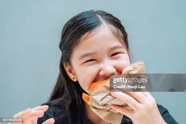 cropped shot of lovely little asian girl enjoying having burger in restaurant. eating out lifestyle. - little burger stock pictures, royalty-free photos & images