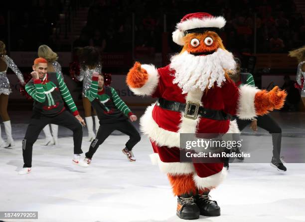 Gritty, the mascot of the Philadelphia Flyers, preforms on the ice during a pregame holiday performance with the Flyers Dance Team prior to an NHL...