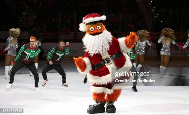 Gritty, the mascot of the Philadelphia Flyers, preforms on the ice during a pregame holiday performance with the Flyers Dance Team prior to an NHL...
