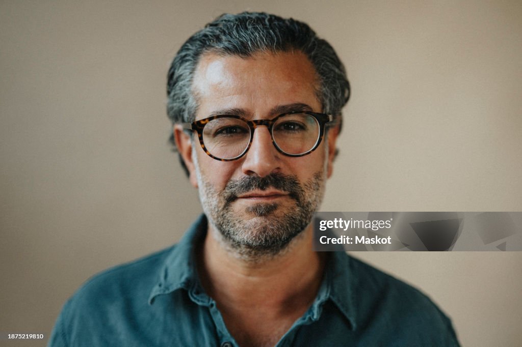 Portrait of mature man with stubble wearing eyeglasses against beige wall