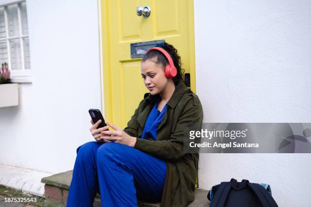 female healthcare professional using her cellphone while sitting on the street - urban life stock pictures, royalty-free photos & images